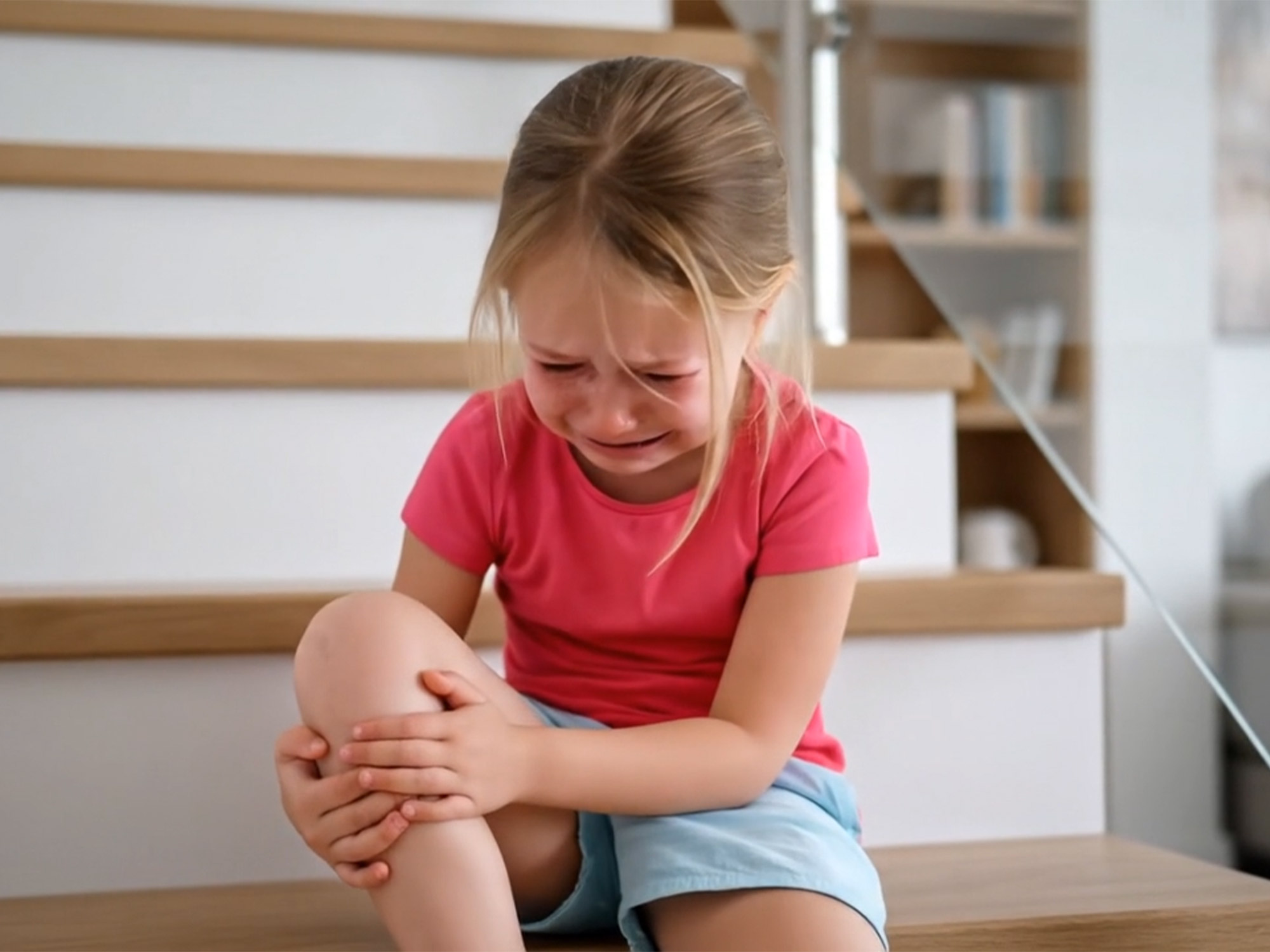 Weinendes kleines Mädchen sitzt auf einer Treppe und hält sich schmerzend das Knie – Beispielbild zur Rutschgefahr ohne Stufenmatten.