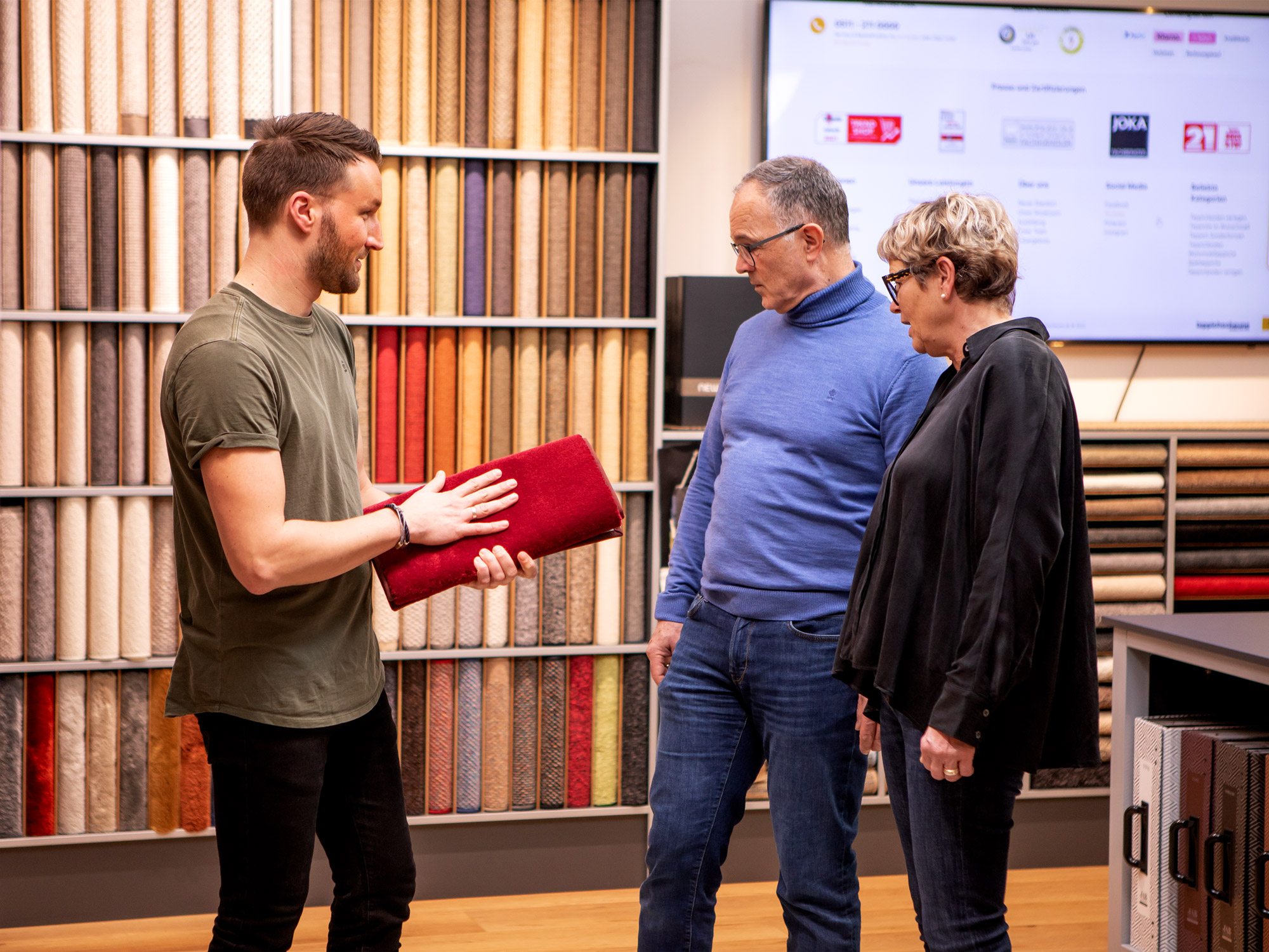 Fachberater zeigt einem Paar im Showroom verschiedene Teppichmuster und berät bei der Auswahl