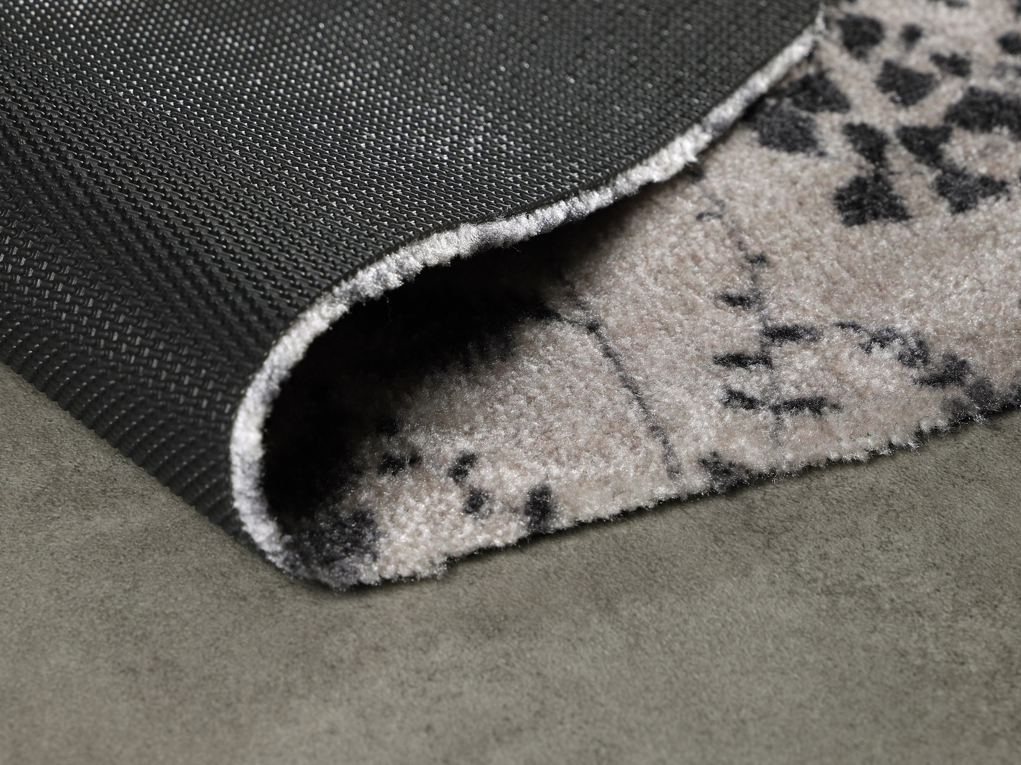 Detailansicht der Ruxedo Fußmatte Lilou Woods mit sichtbar umgeschlagener rutschhemmender Rückseite und dezenter Musterung auf grauem Boden.