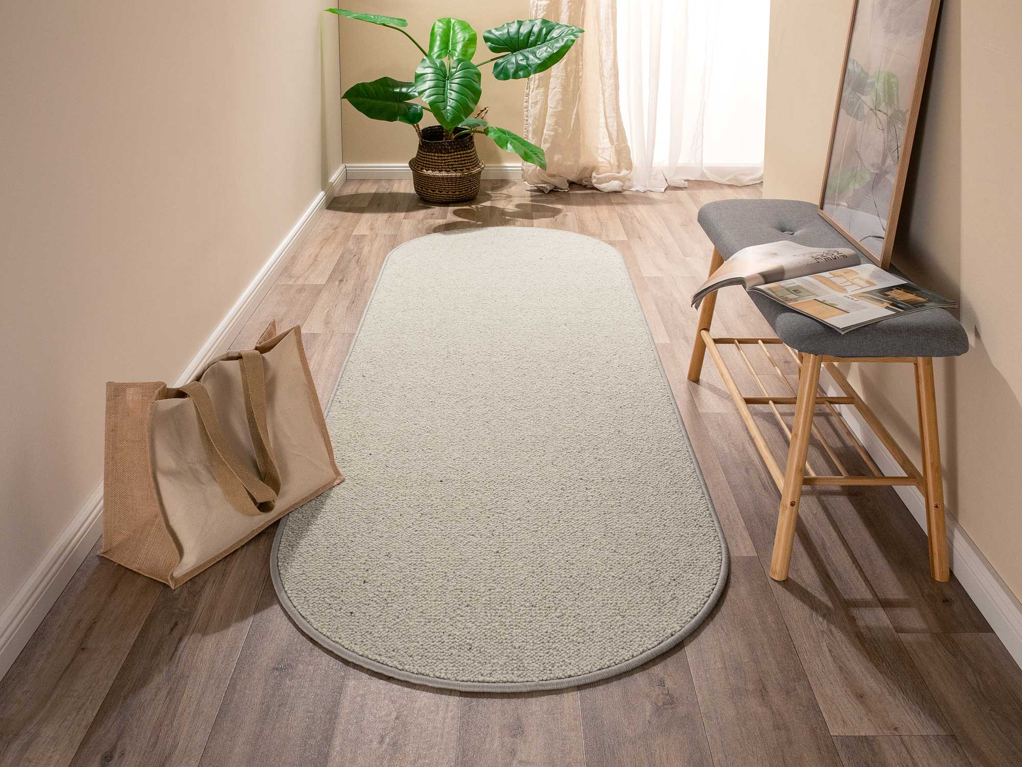 Ovalt geformter Wollteppich Tarfaya in Greige liegt im hellen Flur mit Holzboden, Bank, Pflanze und Stofftasche