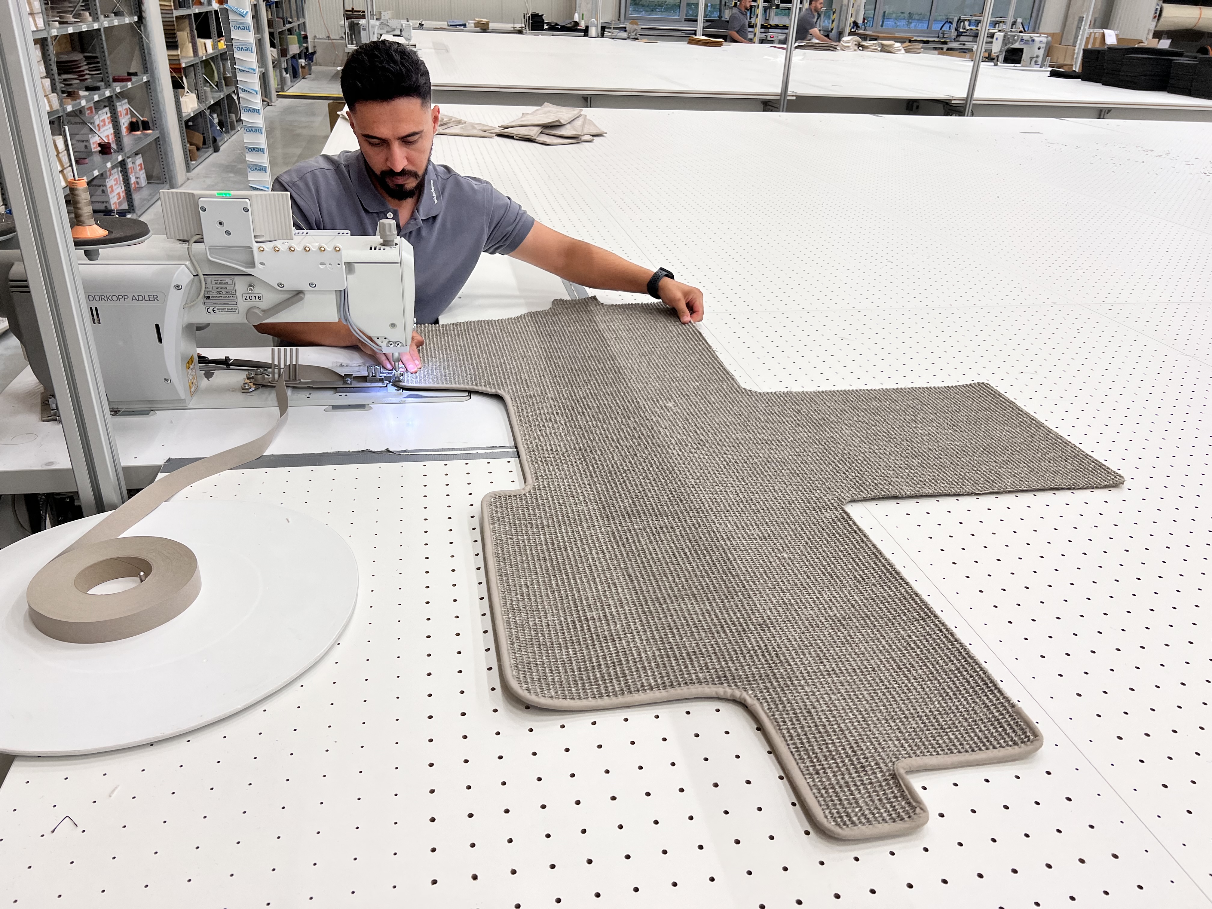 Mitarbeiter näht einen individuell zugeschnittenen Wohnmobilteppich in der Ruxedo-Teppichwerkstatt an einer Industrienähmaschine