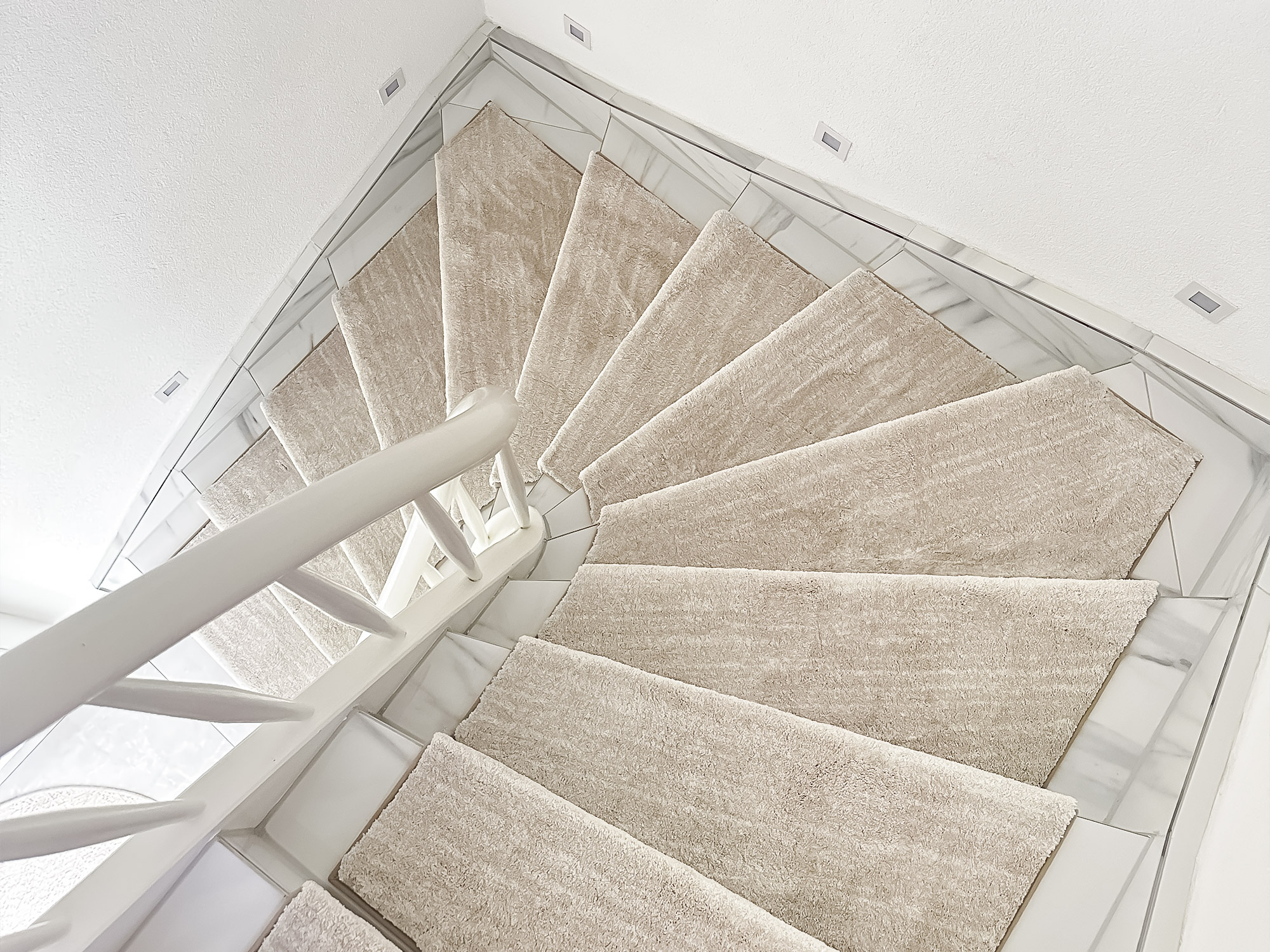 Wendeltreppe mit hellbeigen Ruxedo-Stufenmatten „Carlotta“ aus Hochflor, die für rutschfesten und weichen Tritt auf weißen Stufen sorgen.
