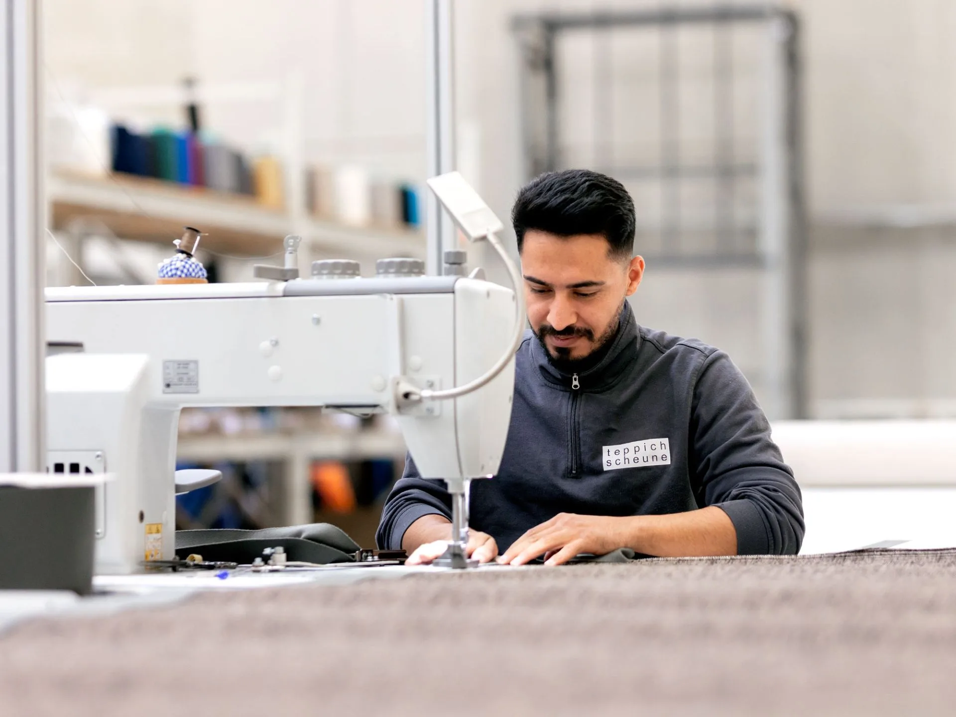 Mitarbeiter der Teppichscheune näht eine Teppichkante an einer Industrienähmaschine – Detailaufnahme aus der Fertigung