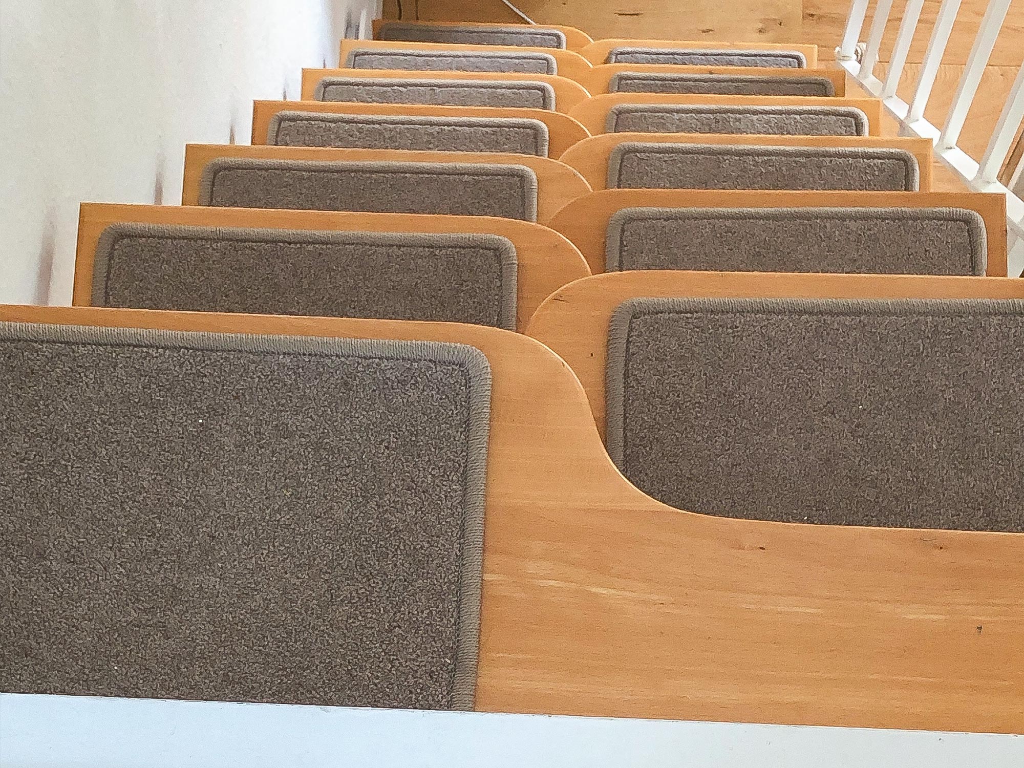 Mehrere rechteckige Stufenmatten in Beige sind sauber und gleichmäßig auf einer Holztreppe angebracht.