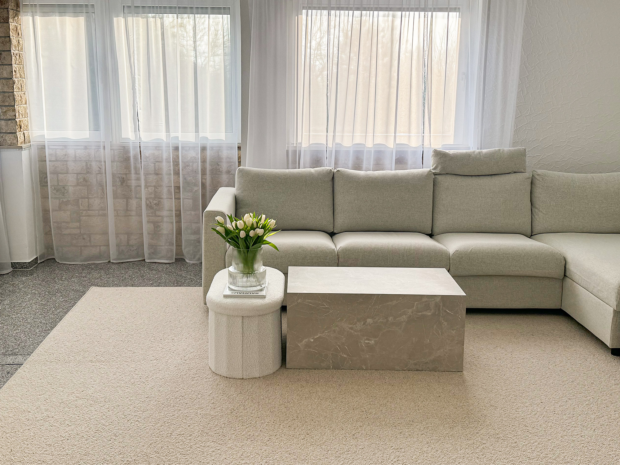 Rechteckiger Wollteppich Tarfaya in Greige im modernen Wohnzimmer mit heller Eckcouch, Marmortisch und Tulpenvase