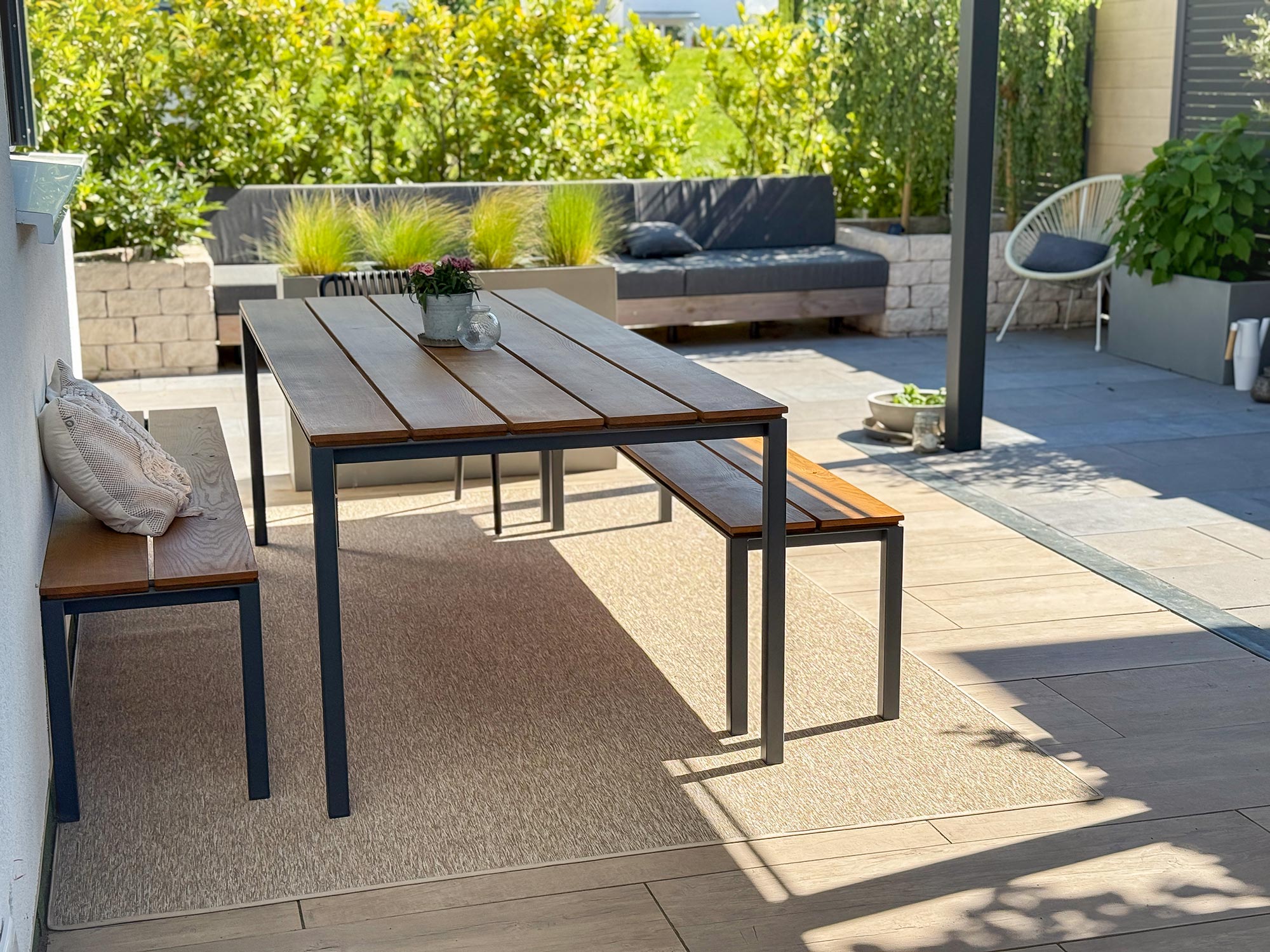 Rechteckiger Outdoorteppich Grenada in Creme von Ruxedo unter Esstisch auf moderner Terrasse mit Sitzbank und Gartenmöbeln