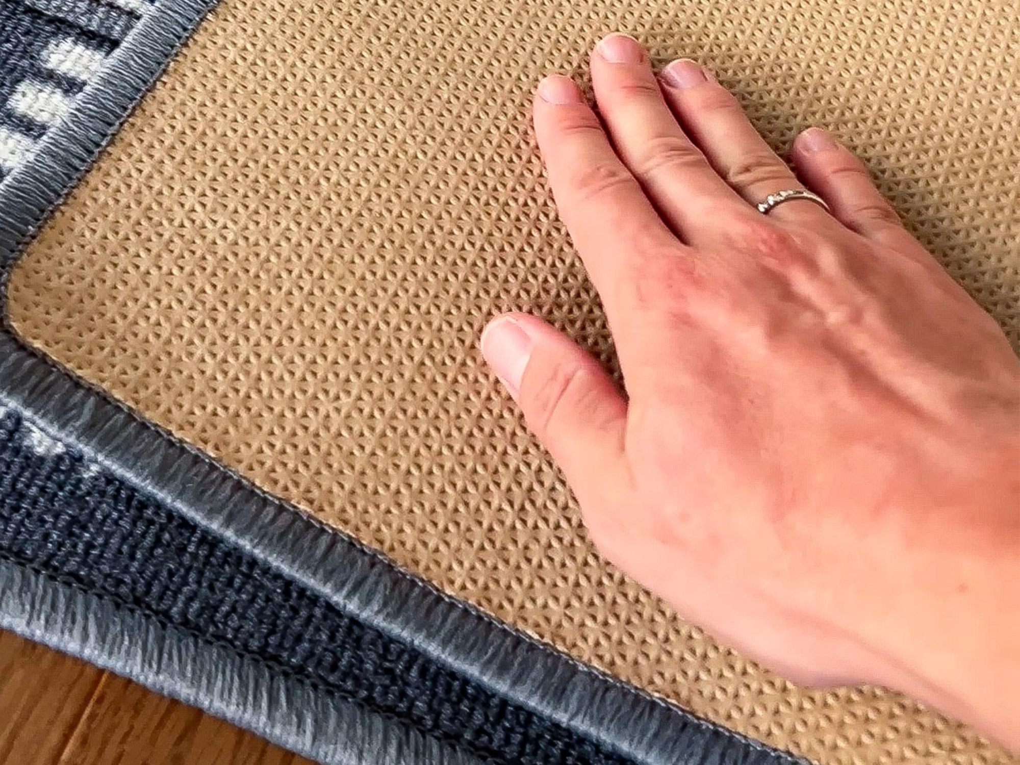 Detailaufnahme der rutschhemmenden Unterseite des Kinderteppichs Greenfield City mit Hand zur Veranschaulichung der Struktur