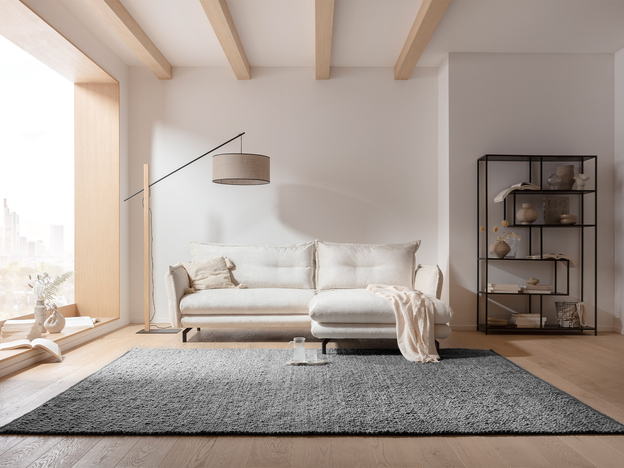 Wohnzimmer mit Ruxedo-Handwebteppich Madita aus Schurwolle in Grau, platziert vor einer hellen Couch und großen Fenstern