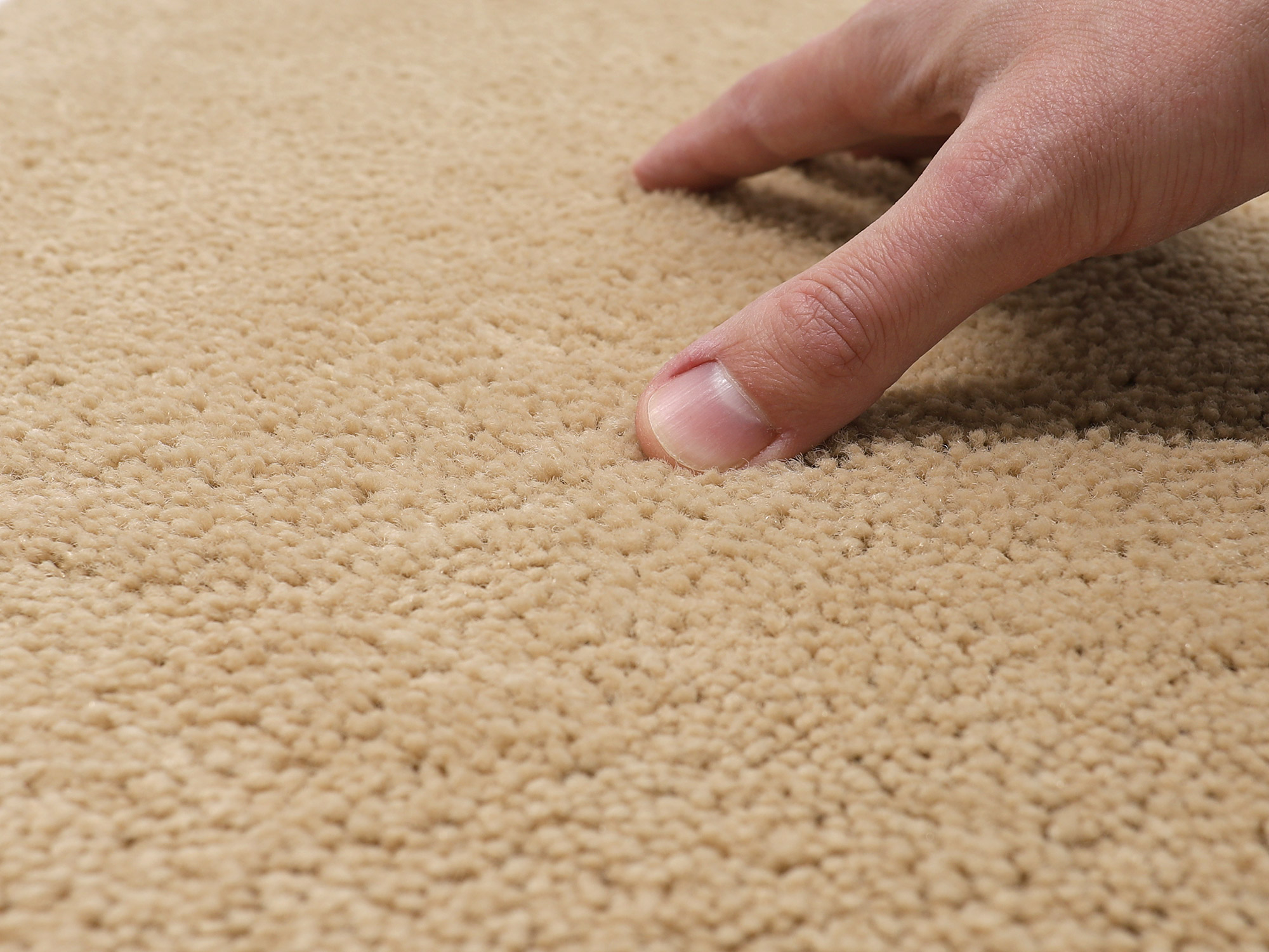 Hand drückt auf den beigen Flor der Ruxedo Fußmatte Romus in einer Detailaufnahme.