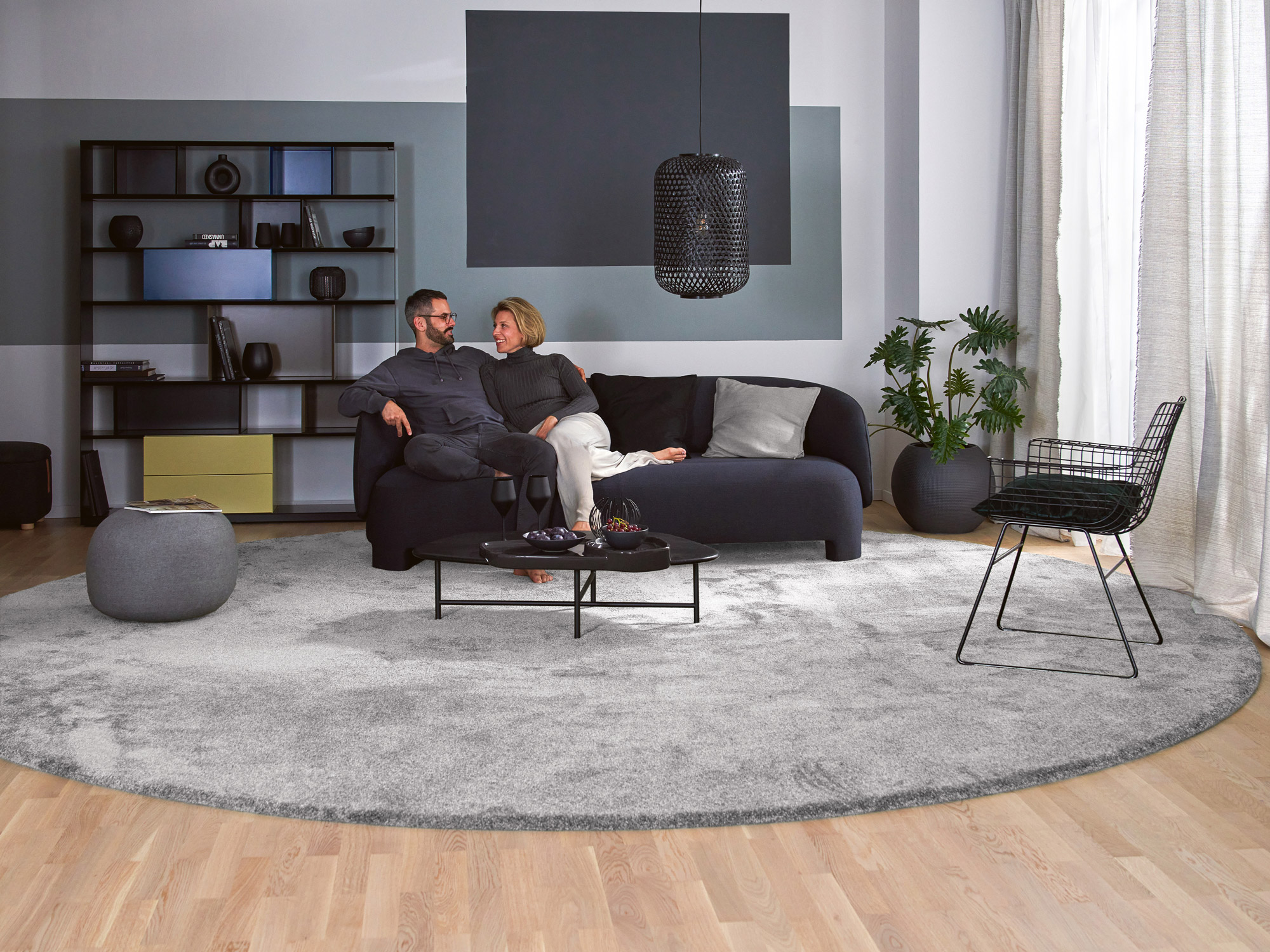 Runder Hochflorteppich Brienne in Silbergrau von Ruxedo im modernen Wohnzimmer mit dunkelblauer Couch und Holzboden